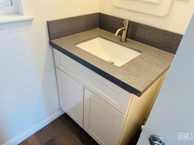 bathroom featuring a textured wall, vanity, baseboards, and wood finished floors