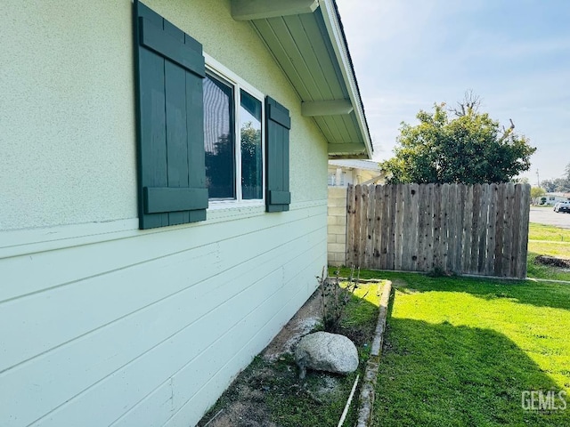 view of home's exterior with stucco siding, fence, and a yard