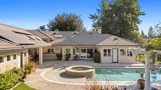 back of house featuring a swimming pool with hot tub, solar panels, and a patio area