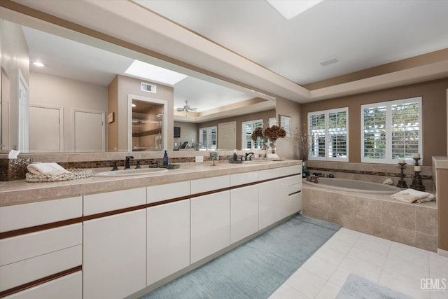 bathroom with a tray ceiling, ceiling fan, vanity, and a relaxing tiled tub