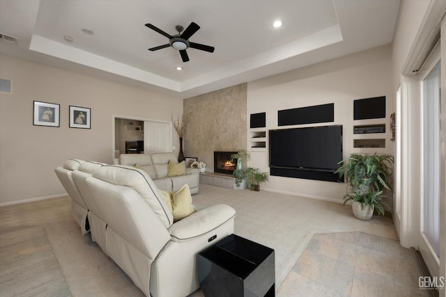 living room with a raised ceiling, built in shelves, ceiling fan, and a fireplace