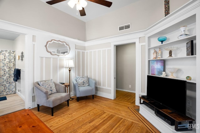 living area with a ceiling fan, visible vents, and wood finished floors