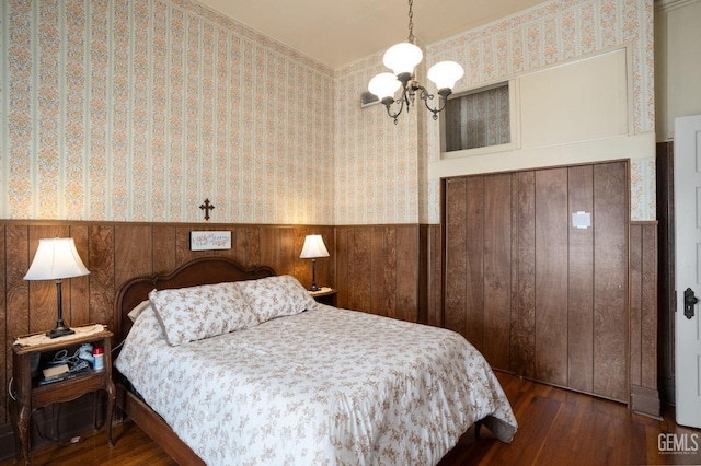 bedroom featuring dark wood-style floors, wainscoting, wood walls, a chandelier, and wallpapered walls