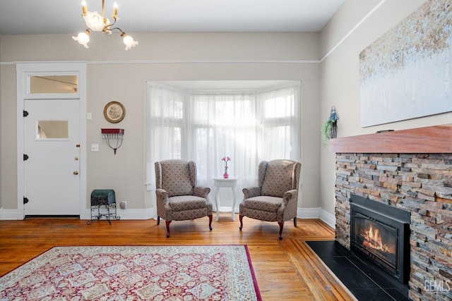 sitting room with an inviting chandelier, baseboards, wood finished floors, and a stone fireplace