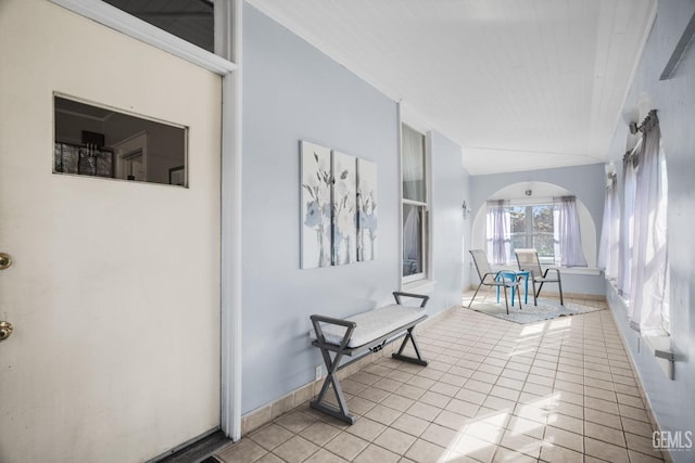 hallway featuring arched walkways, light tile patterned floors, and baseboards