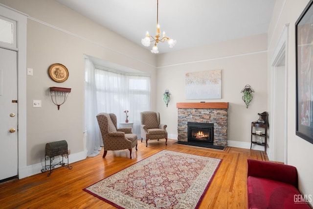 sitting room with a notable chandelier, a stone fireplace, baseboards, and wood finished floors