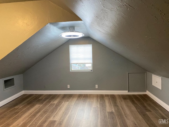 additional living space featuring dark wood-style floors, a textured ceiling, lofted ceiling, and baseboards