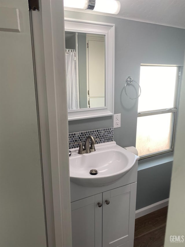 full bathroom featuring baseboards, wood finished floors, vanity, and decorative backsplash