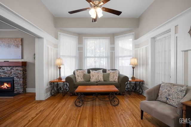 living room featuring light wood-style floors, ceiling fan, baseboards, and a stone fireplace