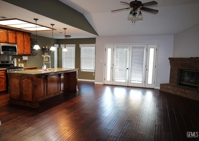 kitchen with pendant lighting, a kitchen island with sink, stainless steel appliances, tasteful backsplash, and dark hardwood / wood-style flooring