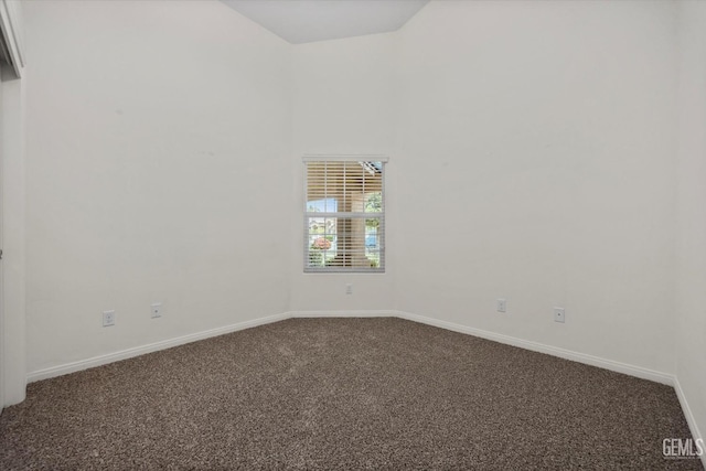 spare room featuring dark colored carpet, baseboards, and a towering ceiling
