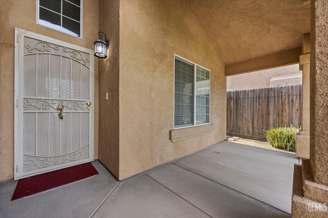 view of exterior entry with stucco siding, a patio area, and fence