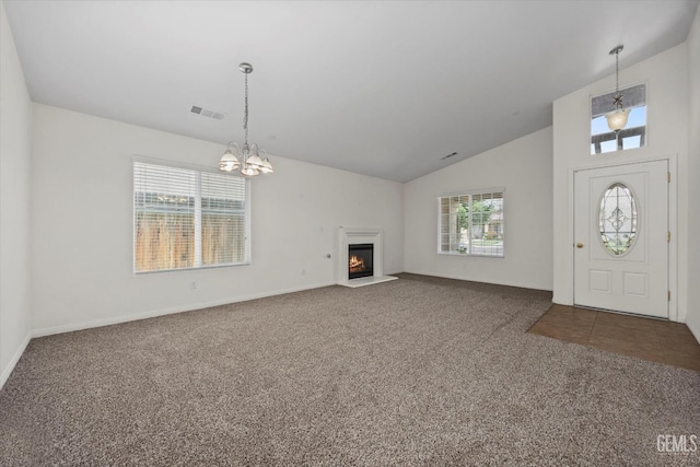 unfurnished living room with carpet flooring, a notable chandelier, high vaulted ceiling, a glass covered fireplace, and visible vents