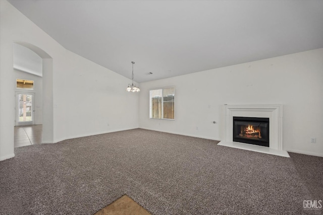unfurnished living room with lofted ceiling, light colored carpet, arched walkways, a fireplace with flush hearth, and a notable chandelier