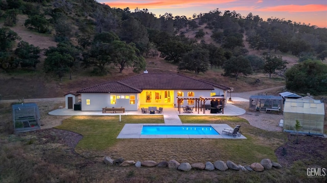 back house at dusk with an outdoor structure, a yard, and a patio