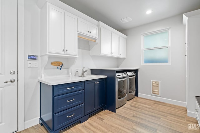laundry area featuring washing machine and clothes dryer, a sink, light wood-style floors, cabinet space, and baseboards