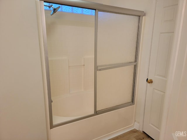 bathroom featuring hardwood / wood-style flooring and bath / shower combo with glass door