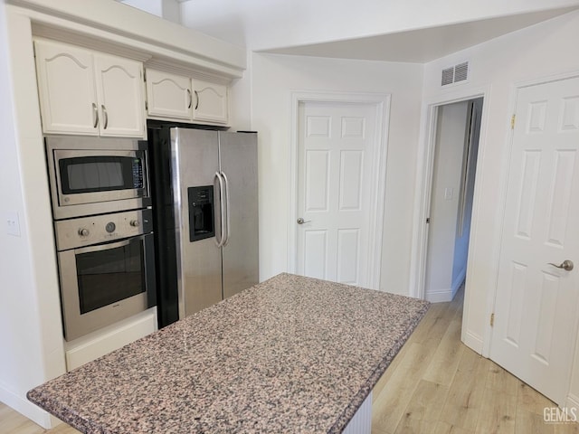 kitchen with white cabinetry, stainless steel appliances, dark stone countertops, and light wood-type flooring