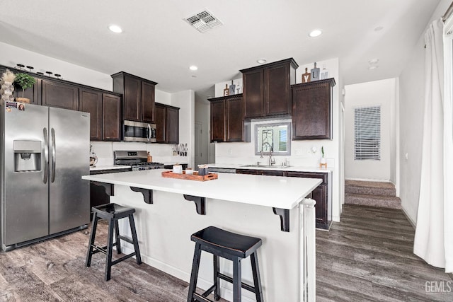5906 Commonwealth Ave, Bakersfield, CA 93313 - kitchen featuring appliances with stainless steel finishes, dark wood-type flooring, dark brown cabinets, a breakfast bar area, and a center island