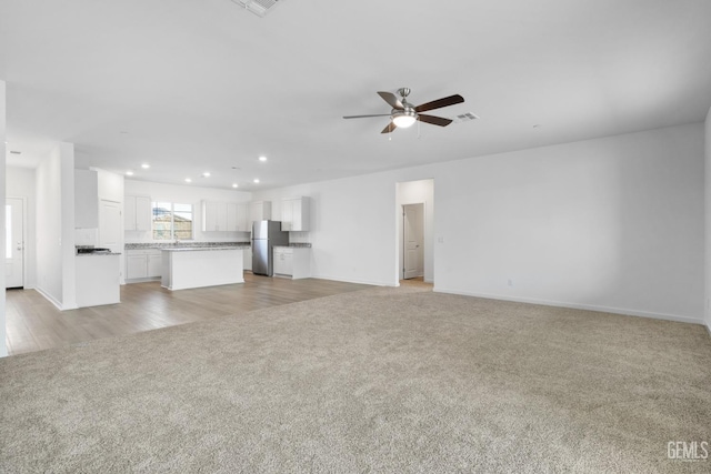 unfurnished living room with light colored carpet and ceiling fan