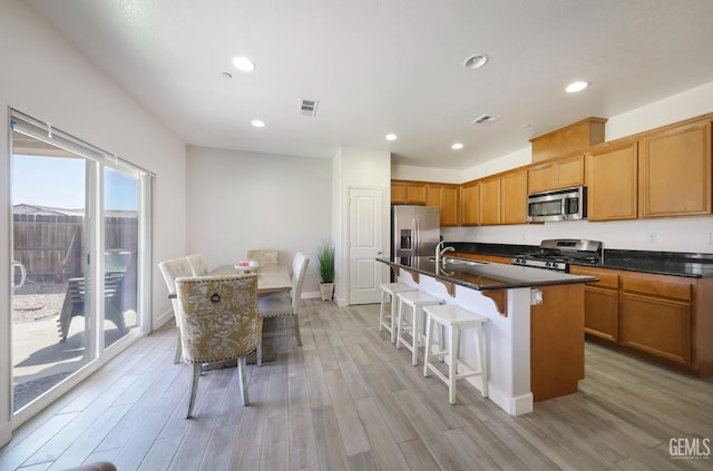 5812 Turquoise Ridge Dr, Bakersfield, CA 93313 - kitchen with stainless steel appliances, dark countertops, light wood-style flooring, a breakfast bar area, and recessed lighting