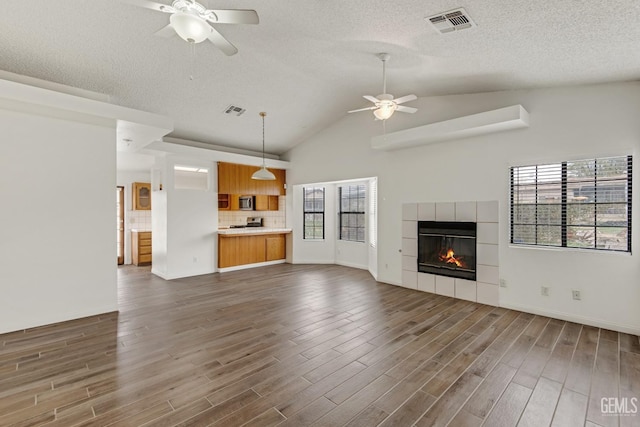 unfurnished living room featuring ceiling fan, dark hardwood / wood-style floors, lofted ceiling, a textured ceiling, and a tiled fireplace