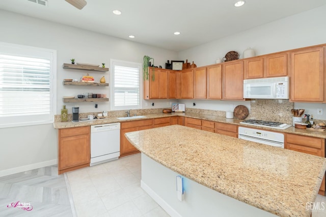 kitchen with white appliances, a center island, light stone counters, and sink