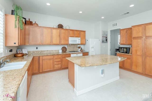 kitchen with white appliances, sink, a kitchen island, light stone countertops, and a healthy amount of sunlight