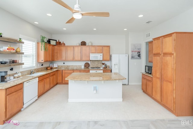 kitchen featuring ceiling fan, a center island, light stone countertops, sink, and white appliances