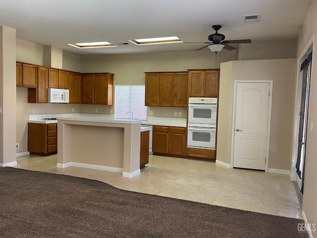11016 Snowcreek Falls Ave, Bakersfield, CA 93312 - kitchen featuring white appliances, brown cabinetry, tile countertops, and a kitchen island