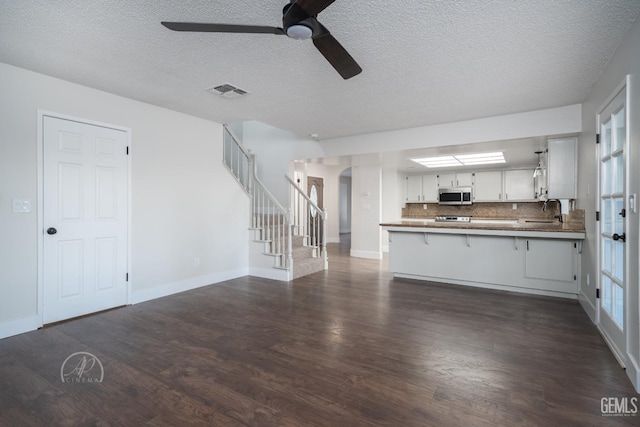 unfurnished living room with dark wood-type flooring, ceiling fan, sink, and a textured ceiling