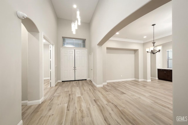 entryway with arched walkways, light wood-type flooring, an inviting chandelier, and baseboards