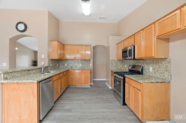3406 Kimmie Rachelle Ct, Bakersfield, CA 93313 - kitchen with appliances with stainless steel finishes, arched walkways, light stone counters, a sink, and decorative backsplash