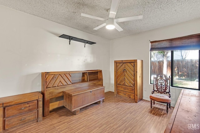 sitting room with baseboards, ceiling fan, light wood-style flooring, and a textured ceiling