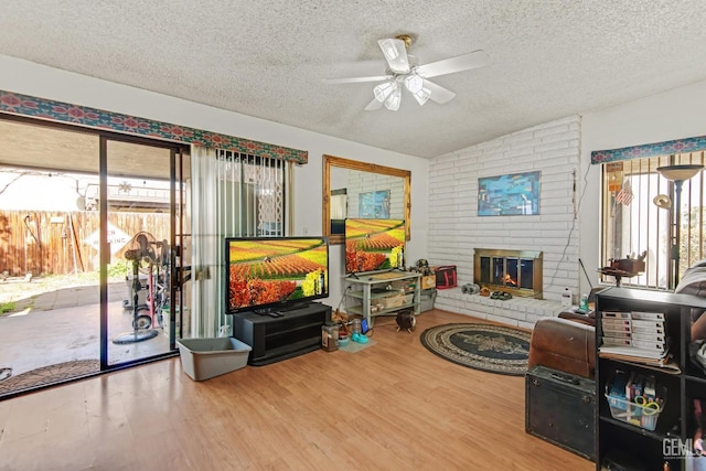 living room with a brick fireplace, ceiling fan, a textured ceiling, and wood finished floors