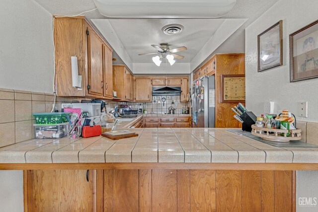 kitchen with a peninsula, visible vents, brown cabinets, tasteful backsplash, and stainless steel fridge