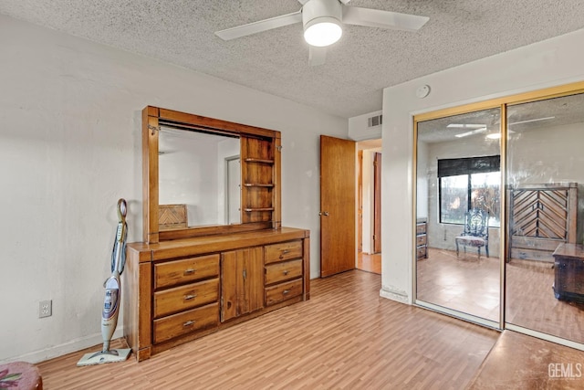 bedroom with light wood-type flooring, a ceiling fan, visible vents, and a textured ceiling