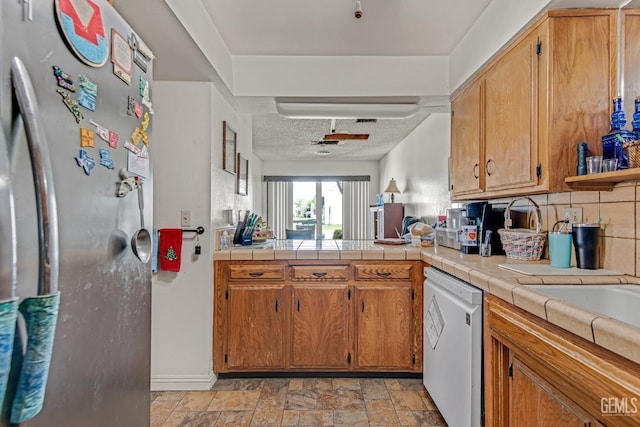 kitchen with decorative backsplash, dishwasher, stone finish floor, freestanding refrigerator, and a textured ceiling