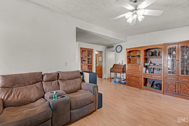 living room with light wood-style flooring, visible vents, ceiling fan, and a textured ceiling