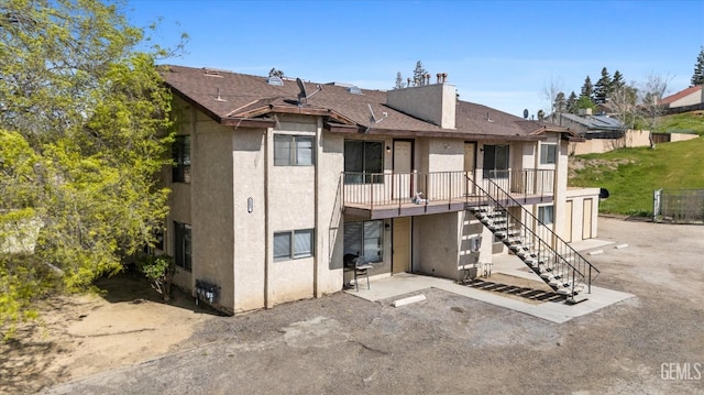 rear view of house featuring stucco siding, a patio area, a chimney, and stairway