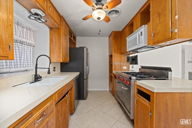 kitchen featuring appliances with stainless steel finishes, ceiling fan, sink, light tile patterned floors, and tile counters