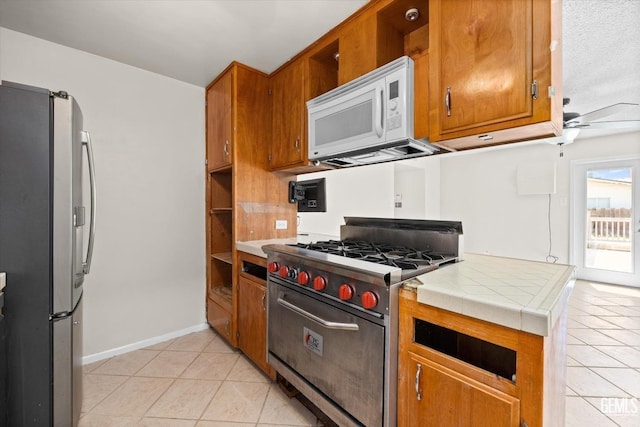 kitchen featuring ceiling fan, a textured ceiling, appliances with stainless steel finishes, tile counters, and light tile patterned flooring