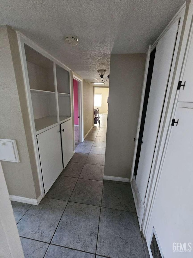 hall featuring visible vents, baseboards, a textured ceiling, and dark tile patterned flooring