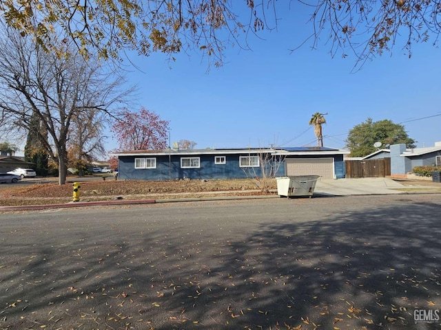 view of front of home featuring concrete driveway, an attached garage, fence, and roof mounted solar panels