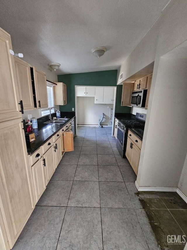 kitchen featuring dark countertops, a sink, appliances with stainless steel finishes, a textured ceiling, and dark tile patterned flooring