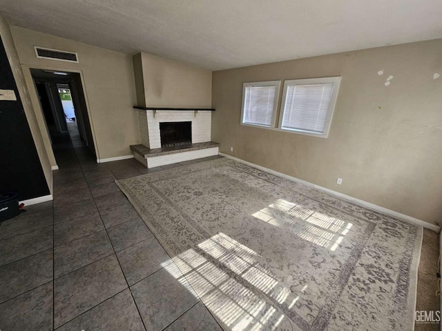 unfurnished living room with visible vents, a fireplace, baseboards, and dark tile patterned flooring