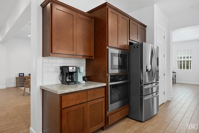 9003 Del Palma Dr, Bakersfield, CA 93314 - kitchen featuring appliances with stainless steel finishes, light wood-style floors, light stone countertops, backsplash, and brown cabinets