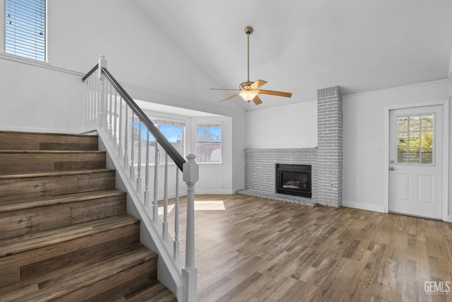 staircase with lofted ceiling, a healthy amount of sunlight, wood finished floors, and a fireplace