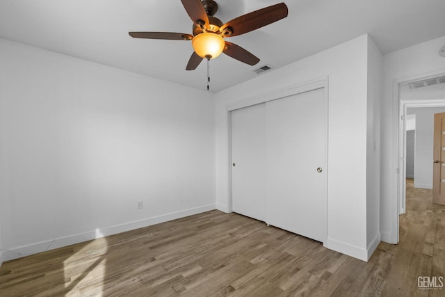 unfurnished bedroom with wood finished floors, visible vents, a closet, and baseboards