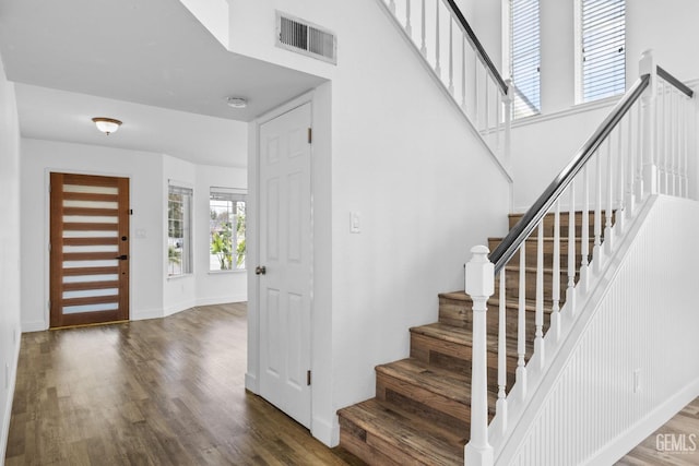 entryway with visible vents, baseboards, wood finished floors, and a towering ceiling